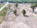 Aerial view of a spacious empty plot of land with few trees and surrounding greenery