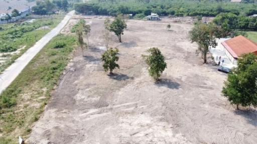 Aerial view of a spacious empty plot of land with few trees and surrounding greenery