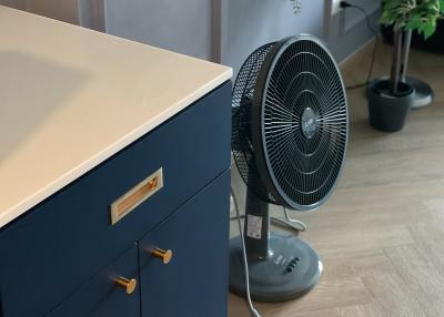 Stylish navy blue nightstand with gold handles next to a black oscillating fan in a modern bedroom
