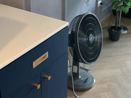 Stylish navy blue nightstand with gold handles next to a black oscillating fan in a modern bedroom