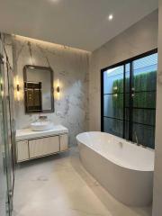 Modern bathroom with marble walls, freestanding tub, and glass shower