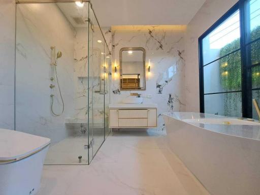 Modern bathroom with marble walls and floors, glass shower enclosure, and standalone bathtub
