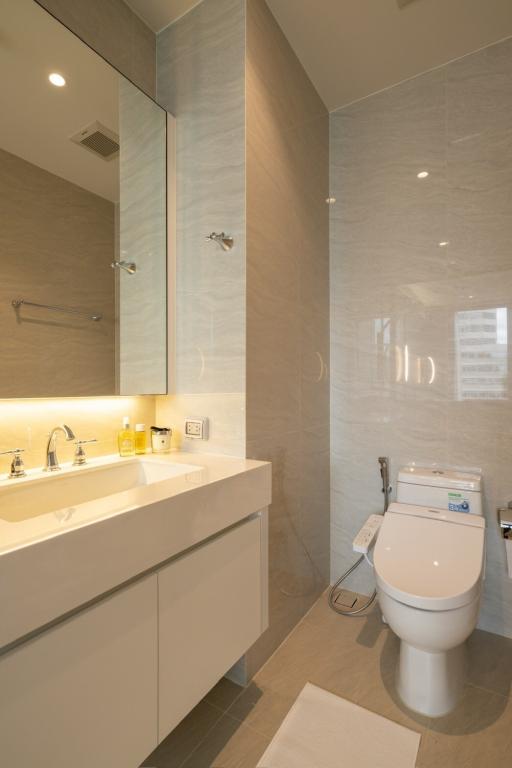 Modern bathroom with neutral tones featuring a vanity sink, toilet, and glass shower enclosure