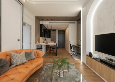 Modern living room with open kitchen design, featuring a leather sofa and flat-screen TV