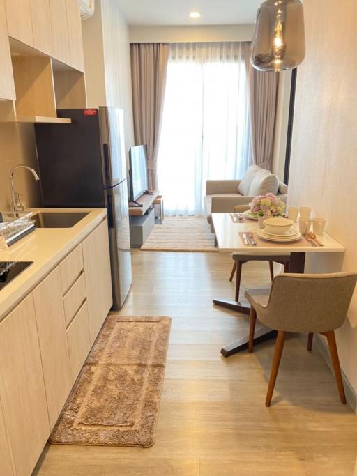 Modern open-plan kitchen with adjoining living room featuring a dining area, natural lighting, wooden flooring, and contemporary furnishings