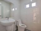 Modern white tiled bathroom with a sink, toilet, and shower