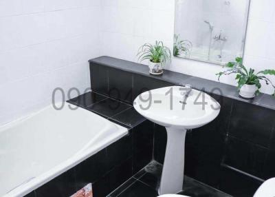 Modern white tiled bathroom with a bathtub, sink, toilet, and decorative plants