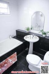 Modern white tiled bathroom with a bathtub, sink, toilet, and decorative plants