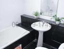 Modern white tiled bathroom with a bathtub, sink, toilet, and decorative plants