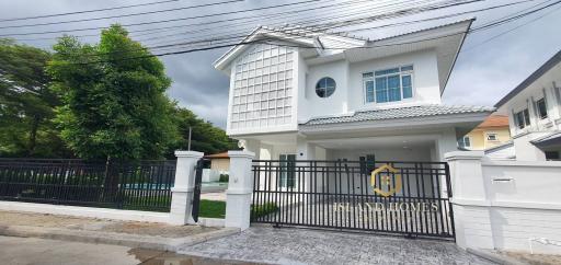White two-story house with a unique window design and gated entrance under a cloudy sky