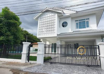 White two-story house with a unique window design and gated entrance under a cloudy sky