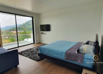 Cozy bedroom with a balcony view, furnished with a large bed, and modern amenities including a flat-screen TV