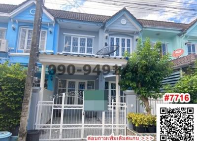 Blue two-story residential townhouse with a white fence, gate, and clear sky