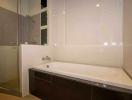 Modern bathroom interior with a clean bathtub, tiled walls, and glass shower partition