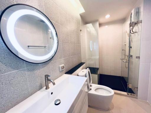 Modern bathroom with a glass shower enclosure, circular mirror, and gray tiles