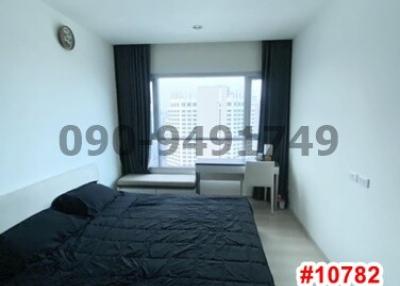Compact bedroom with a double bed, dark linens and a city view from the window