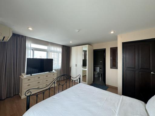 Spacious bedroom with modern furnishings, including a large bed, dresser, and flat-screen TV