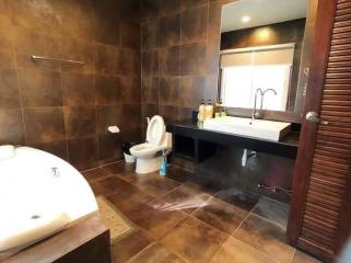 Modern bathroom with dark tile finishing, including a bathtub, sink, and toilet
