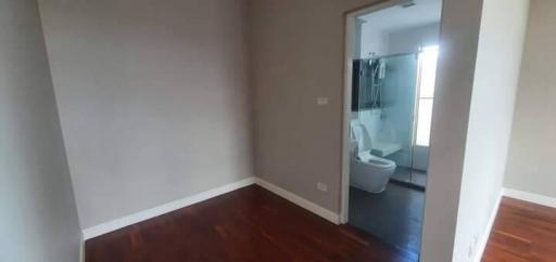 Empty bedroom with polished wooden floor and open bathroom door