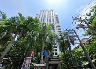 Tall residential building exterior surrounded by lush green trees under a clear blue sky