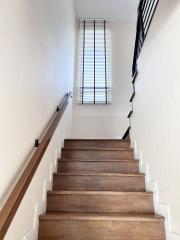 Wooden stairway leading up with white walls and a tall window with blinds