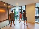 Prospective buyers touring a spacious living room with large windows and adjacent balcony