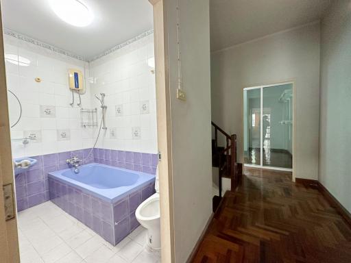 Spacious bathroom with a purple bathtub and modern amenities leading to a wooden staircase
