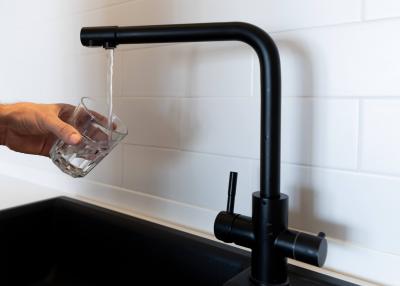 Close-up of a modern kitchen faucet with running water and a hand holding a glass