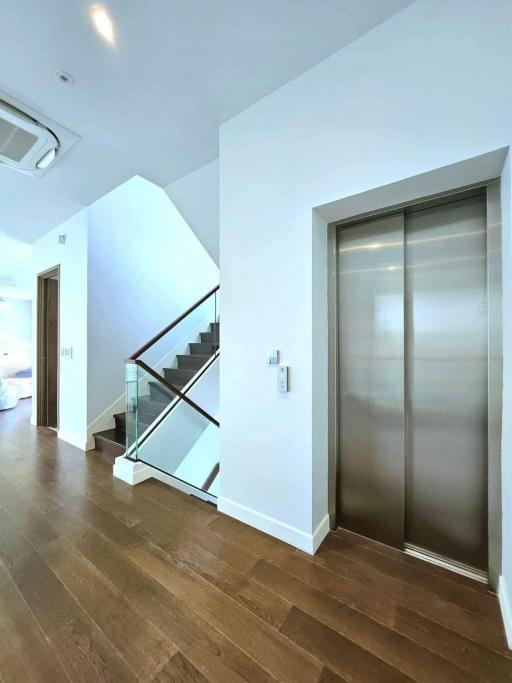 Modern hallway with wooden floors, an elevator, and staircase
