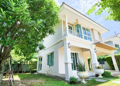 Two-story residential home with a green lawn and lush trees