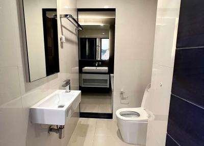 Modern bathroom with white and dark tiling, showing sink, toilet, and mirrored cabinet