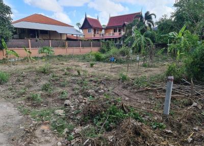 Empty residential plot of land with some vegetation and houses in the background