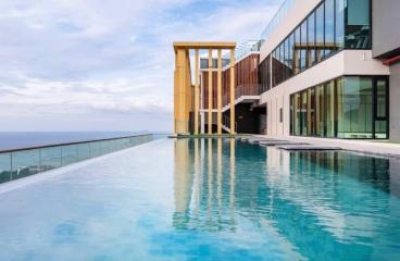 Modern infinity pool with ocean view next to a luxurious building