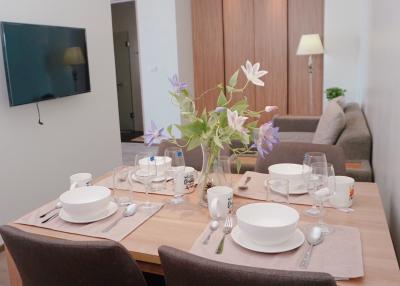 Modern dining area with table set for a meal and open plan living space in the background