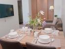 Modern dining area with table set for a meal and open plan living space in the background