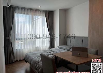 Modern bedroom interior with large bed, grey sofa, wooden table, and a laptop