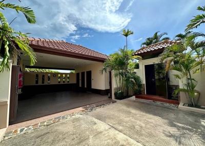 Spacious driveway leading to a single-story house with red tiled roof and tropical landscaping