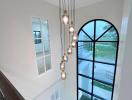 Elegant staircase with cascading pendant lights and large arched window