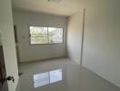 Bright empty bedroom with glossy tiled flooring and a large window