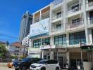 Modern multi-floor buildings with retail space on ground level and parking in front under blue sky