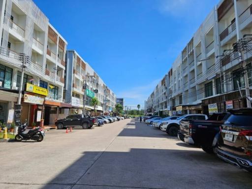 Street view of a row of modern townhouses with commercial spaces on the ground floor under a clear blue sky