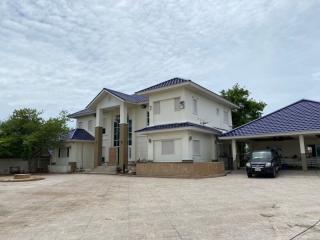 Spacious two-story house with a blue roof and ample parking under a cloudy sky