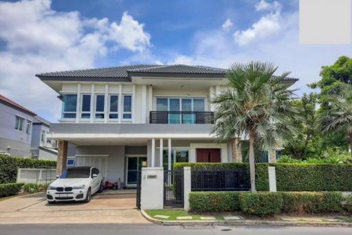 Modern two-story house with a white facade, garage, and lush front yard landscaping