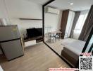 Compact bedroom with modern furnishings, including a bed, desk, television, and refrigerator