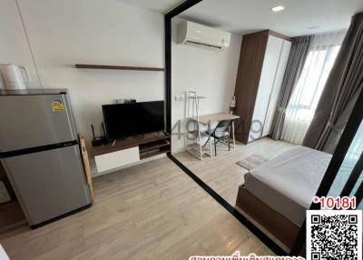 Compact bedroom with modern furnishings, including a bed, desk, television, and refrigerator