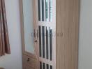 Modern wooden wardrobe in a bedroom setting with visible curtain