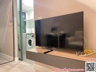 Modern living room with large TV and adjacent laundry appliances