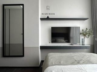Modern bedroom interior with a neatly made bed, a wall-mounted TV, and decorative plants