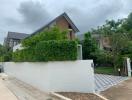 Residential house exterior with a white boundary wall and hedge