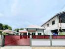 Modern suburban house with red gate and fence under a cloudy sky